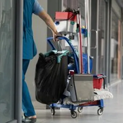 Reinigungskraft schiebt Reinigungswagen mit Müllsack durch Flur