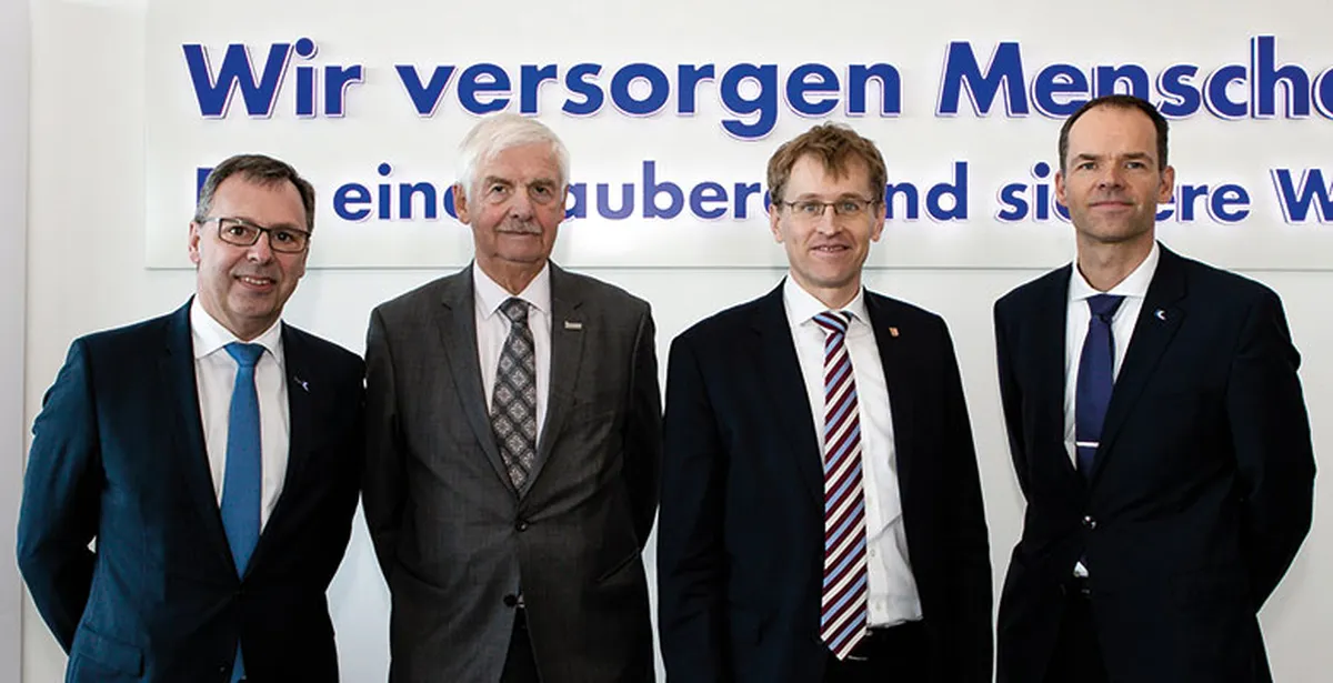 Vier Männer im Anzug vor dem Schriftzug Wir versorgen Menschen
