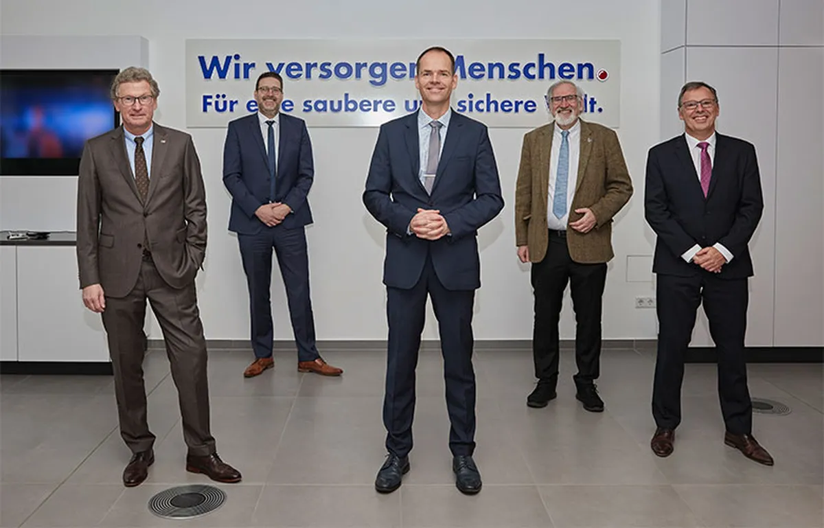 Fünf Männer im Anzug vor dem Schriftzug Wir versorgen Menschen
